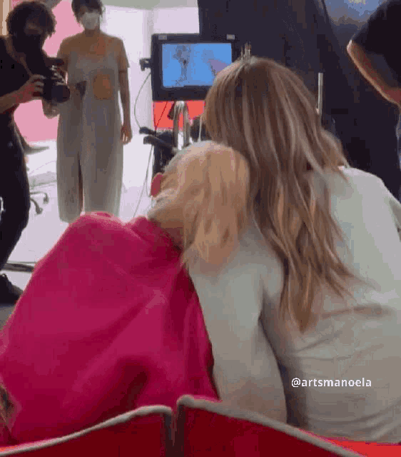 two women are hugging each other in front of a camera with the name artsmanoela written on the bottom