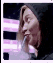 a woman in a hoodie is drinking through a straw from a glass .