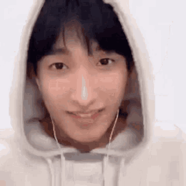 a young man wearing a white hoodie and earphones is smiling .