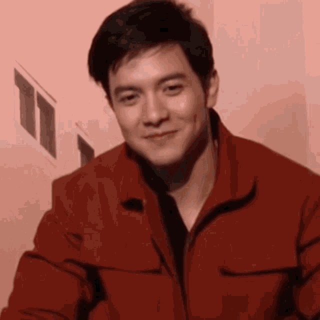 a young man in a red jacket is smiling in front of a pink wall .