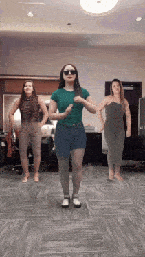 three women are dancing in a room with one wearing a green shirt