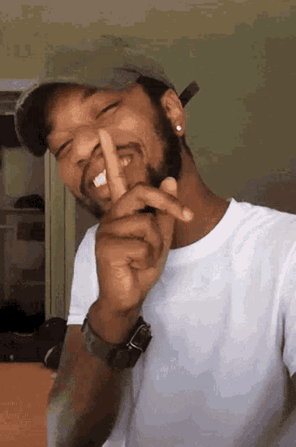 a man wearing a hat and a white shirt is making a shhh gesture with his finger