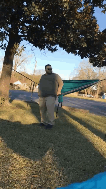 a man in sunglasses stands next to a hammock