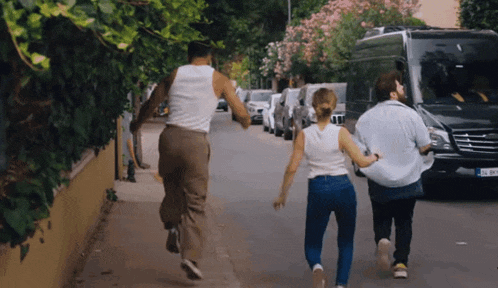 a man and two women are running down a street with a mercedes van behind them
