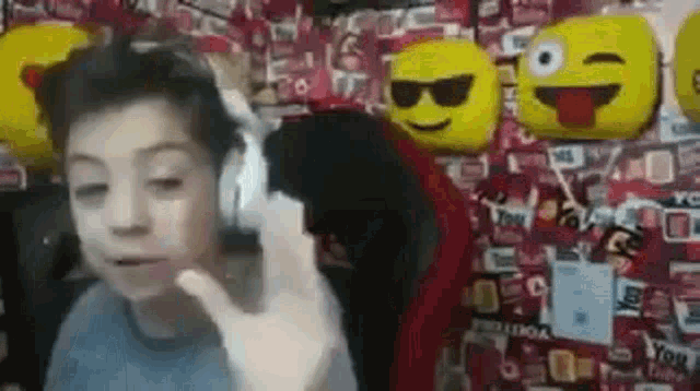 a young boy is wearing headphones and making a funny face in front of a wall with emojis on it .
