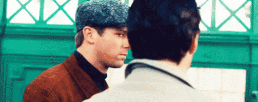 two men are standing next to each other in front of a green wall . one of the men is wearing a hat .