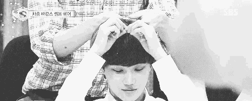a black and white photo of a person putting a wig on a young boy 's head .