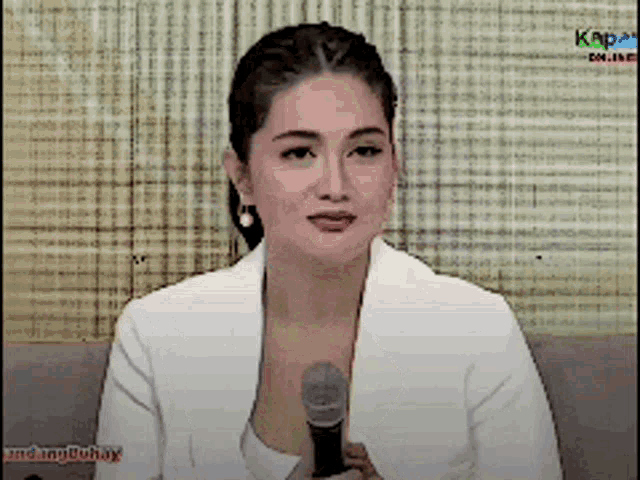 a woman in a white jacket holds a microphone in front of a screen that says kapamilya