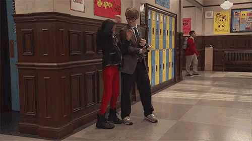 a boy and a girl are walking down a hallway in a school with lockers and a sign that says super hero