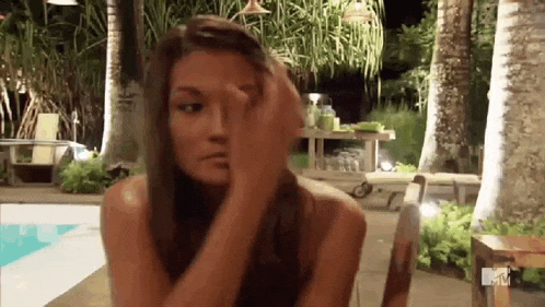 a woman is sitting at a table in front of a pool covering her face with her hand .