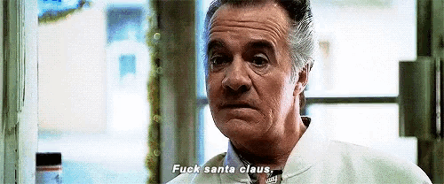 an older man is standing in front of a window talking to santa claus .