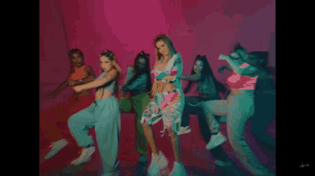 a group of women are dancing in a room with a pink background