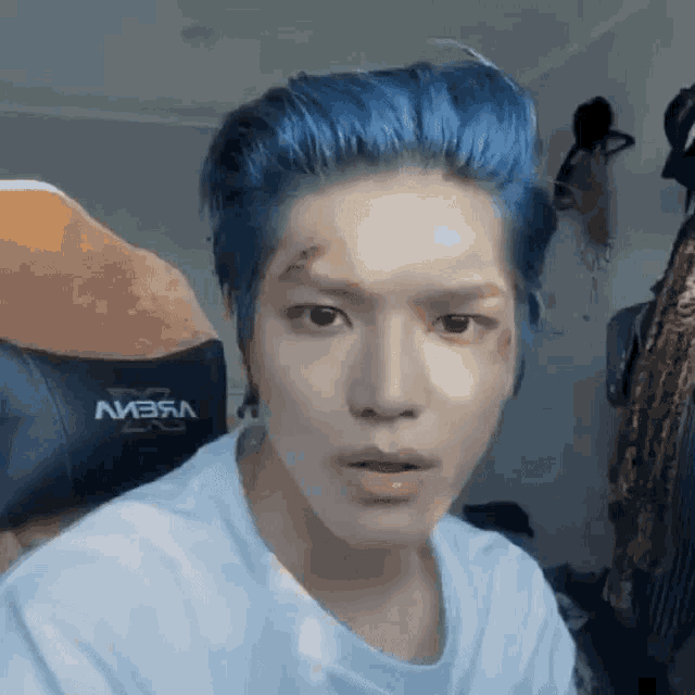a man with blue hair is wearing a white shirt and a black chair .