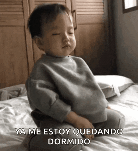 a baby is sitting on a bed and saying ya me estoy quedando dormido .