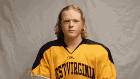 a young man wearing a yellow west virginia jersey salutes
