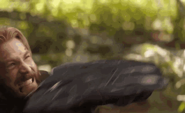 a man with a beard is smiling while holding a sword in a forest .