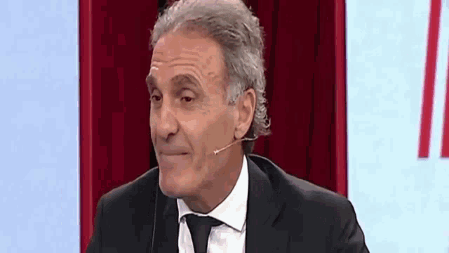 a man in a suit and tie is talking into a microphone on a red background .