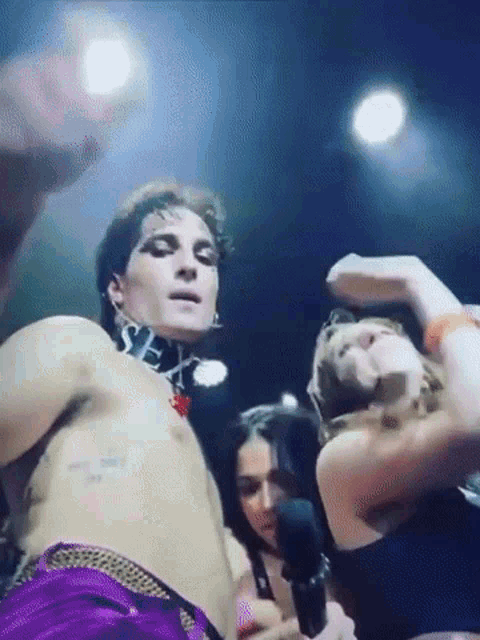 a man without a shirt is dancing on a stage while a woman holds a microphone in front of him .