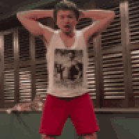 a man in a white tank top and red shorts is standing with his hands on his head