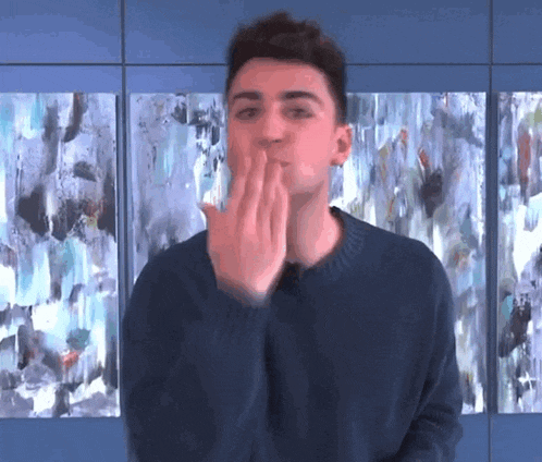 a young man blowing a kiss in front of a wall of paintings