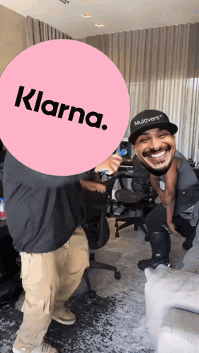 a man wearing a hat that says multiverse is smiling behind a pink sign that says klarna
