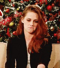 a woman with red hair is sitting in front of a christmas tree and making a sad face