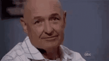 an older bald man is smiling for the camera while wearing a white shirt .
