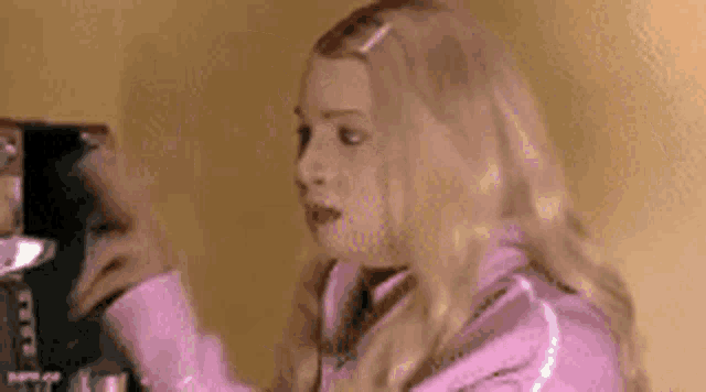 a woman in a pink jacket is standing in front of a mirror and looking at herself .
