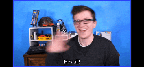 a man wearing glasses says hey all in front of a blue wall