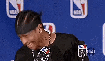 a man wearing a headband and a necklace is smiling while standing in front of a microphone .