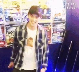 a man in a plaid shirt is standing in front of a wall with posters on it and the word lyrical on the bottom