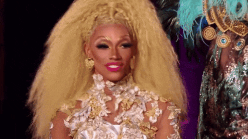 a drag queen with a very long blonde wig is wearing a white and gold dress .