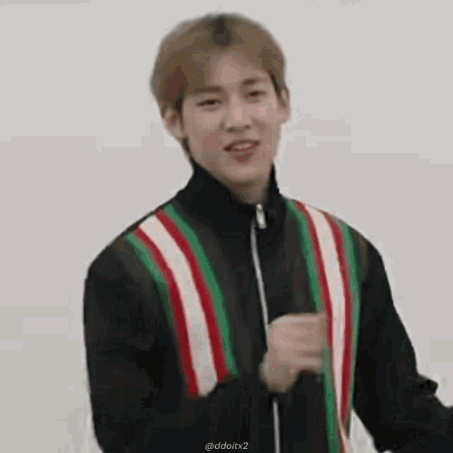 a young man wearing a striped jacket is standing in front of a white wall and making a funny face .