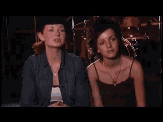 two women are sitting next to each other in front of drums