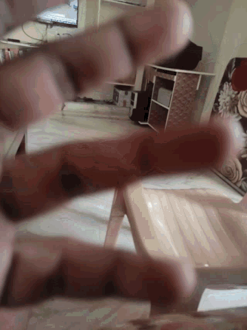a person 's fingers are visible in a blurry photo with a chair in the background