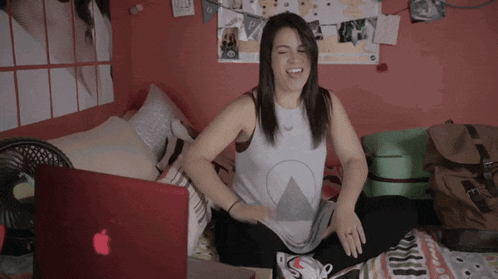 a woman sits on a bed with an apple laptop in front of her