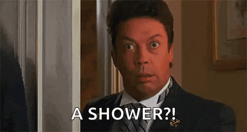 a man in a suit and tie is standing in front of a door and asking for a shower .