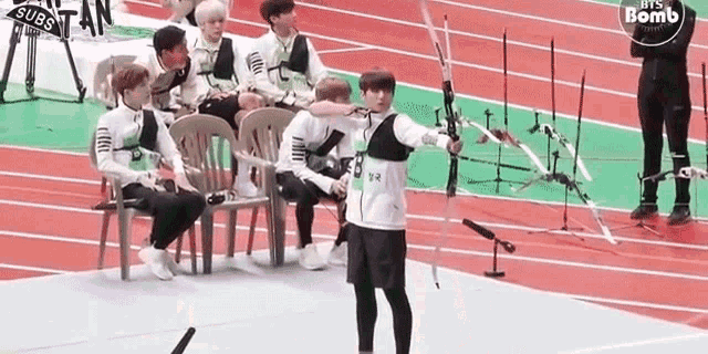 a man is holding a bow and arrow on a track while other people watch .