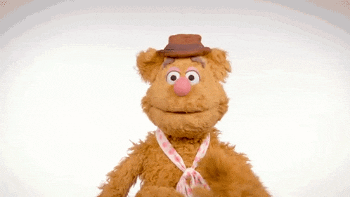 fozzie bear from the muppet show is wearing a hat and tie and waving .