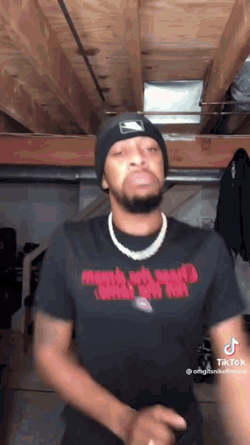 a man wearing a beanie and a t-shirt is standing in a garage .