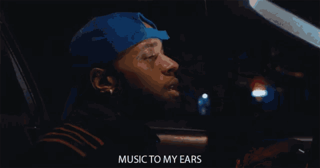 a man in a blue hat is singing music to my ears while sitting in a car .