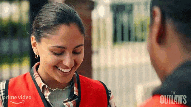 a woman in a red vest is smiling and talking to a man .