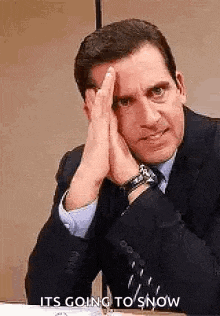 a man in a suit and tie is sitting at a desk with his hands on his forehead .