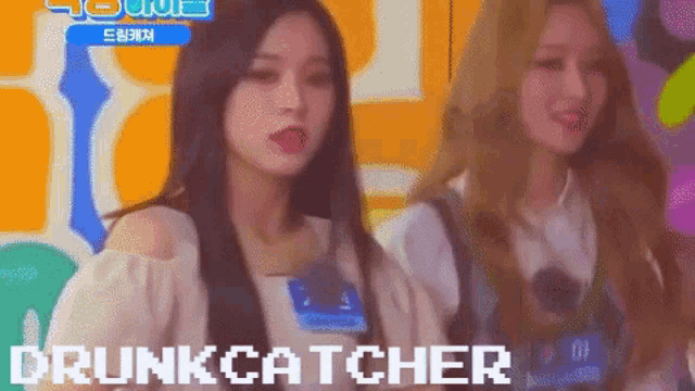 two girls are standing next to each other and the word drunkcatcher is on the screen behind them .