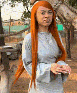 a woman with long red hair is wearing a white dress and a cross necklace .