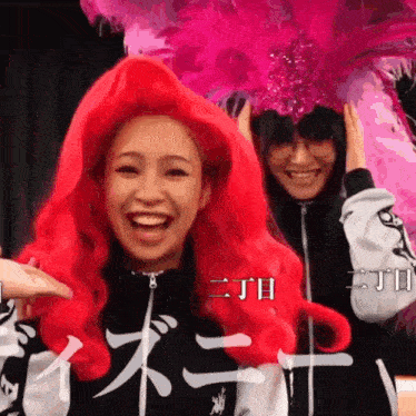 a woman wearing a red wig stands next to another woman wearing a pink hat