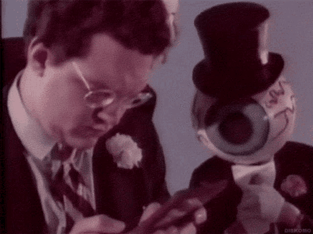 a man in a suit and tie is looking at a puppet with a big eye