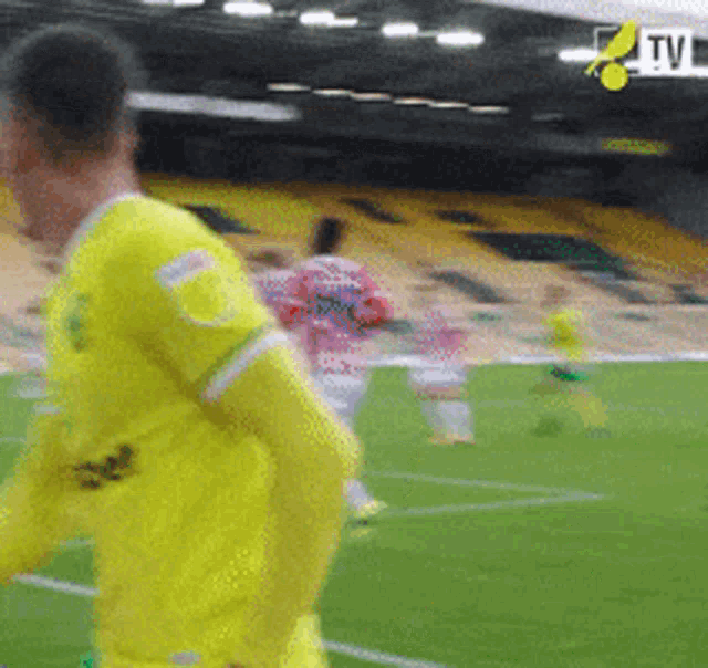 a man in a yellow jersey is running on a soccer field with a tv logo in the background