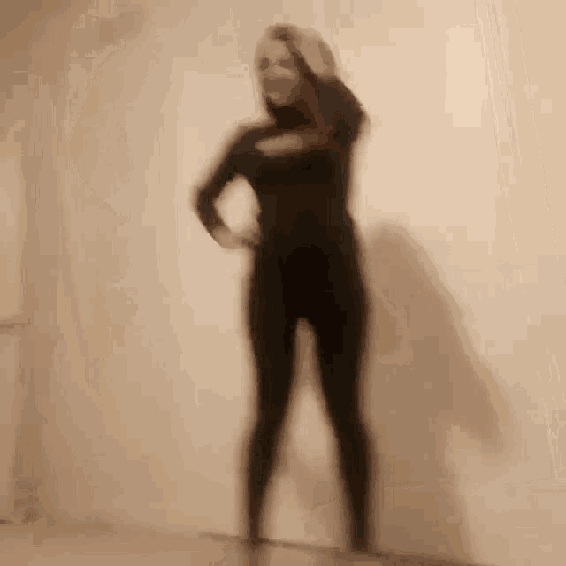 a blurry picture of a woman in a black bodysuit standing in front of a wall .