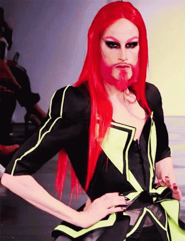 a drag queen with red hair and a beard is on a runway